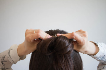 A young woman with brown hair ties her hair into a bun, viewed from the rear. Tutorial photo of simple hairstyle pinned half updo for long hair