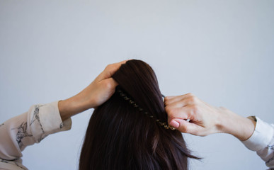 A young woman with brown hair ties her hair into a bun, viewed from the rear. Tutorial photo of simple hairstyle pinned half updo for long hair