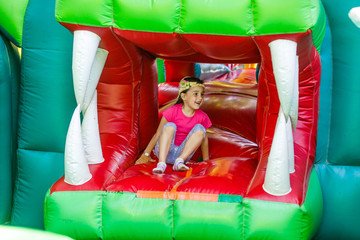 Cute funny preschool little girl in a colorful, jumping and bouncing in an inflatable castle having...
