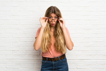 Young blonde woman over white brick wall with glasses