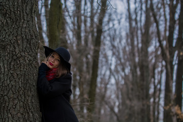 The girl in a black coat, a shovel hat and with red lipstick on lips, walks in the park. Style and modern fashion.