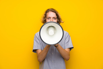 Blonde man over isolated yellow background shouting through a megaphone
