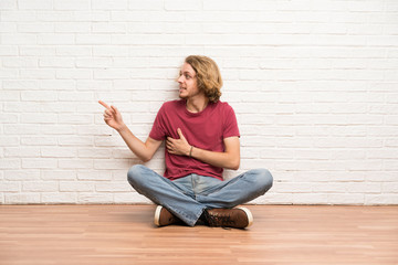 Blonde man sitting on the floor pointing finger to the side