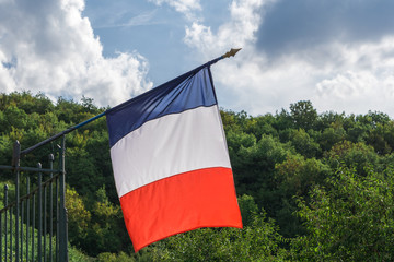 French flag waving in wind on green forest hill and sky with clouds background