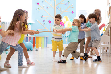 group of preschool kids play and pull rope together in daycare - obrazy, fototapety, plakaty