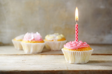 muffins or cupcakes with a pink burning candle on a wooden board against a rustic background, birthday concept with copy space
