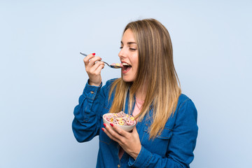 Young woman with bowl of cereals over isolated blue wall