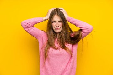 Young woman with long hair over isolated yellow wall frustrated and takes hands on head