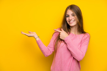 Young woman with long hair over isolated yellow wall holding copyspace imaginary on the palm to insert an ad