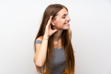 Young woman with long hair over isolated white wall listening to something by putting hand on the ear