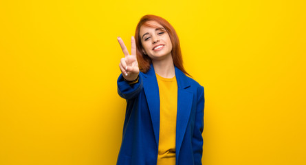 Young redhead woman with trench coat smiling and showing victory sign