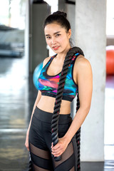 Obraz premium portrait of Beautiful athletic Asian woman posing with battle ropes at sport fitness gym . workout . exercise