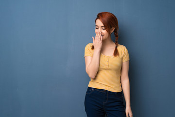 Young redhead woman over blue background posing with arms at hip and laughing