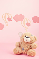 Cute teddy bear over the pink pastel background with clouds and ballons