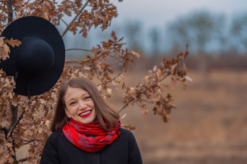 The girl in a black coat, a shovel hat and with red lipstick on lips, walks in the park. Style and...