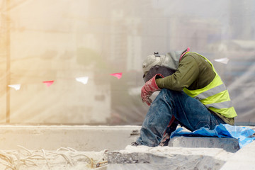 The tired construction worker in the green waistcoat and the red glove sitting in the construction...