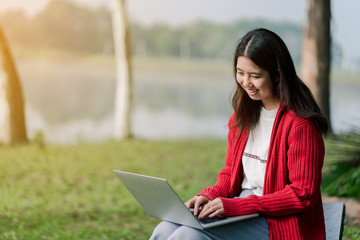 A lovely Asian girl is bright in the tourist area. There is a laptop computer in the hand on the road amid the fog. The back is a lake Sitting looking at the computer screen, working smiling happily