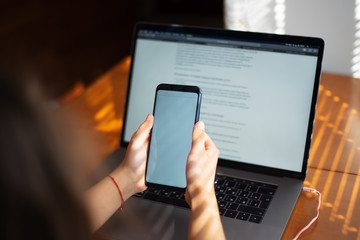 Smartphone in hands over laptop background, on wooden desk