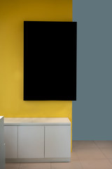 Black mockup frame hanging on yellow wall in modern interior.