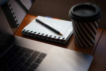 Close-up of laptop, notebook and cup of coffee on wooden desk