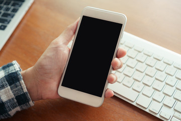 Close up hand using smartphone on desk background in office.  On hand holding smartphone blank display.