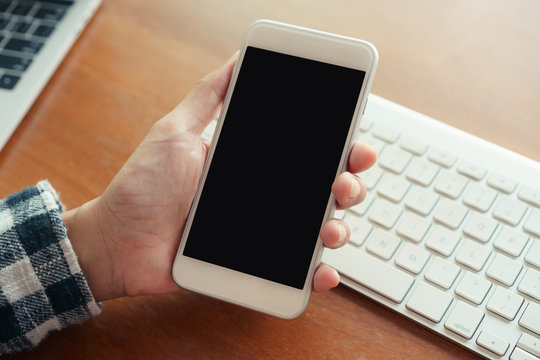 Close Up Hand Using Smartphone On Desk Background In Office.  On Hand Holding Smartphone Blank Display.