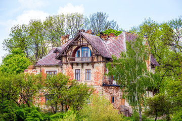 Fototapeta na wymiar Old house in Gothic style among green trees in sunny weather_