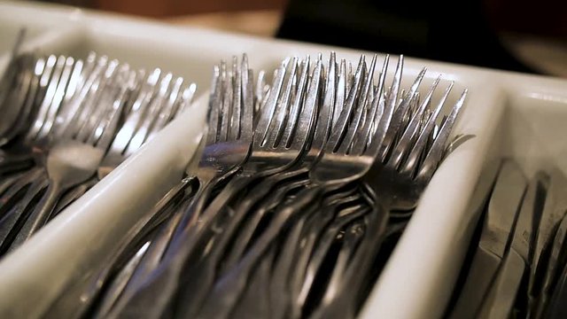 slow pan across stack of silverware. The camera pans left and right across a tray full of knives, forks and spoons.