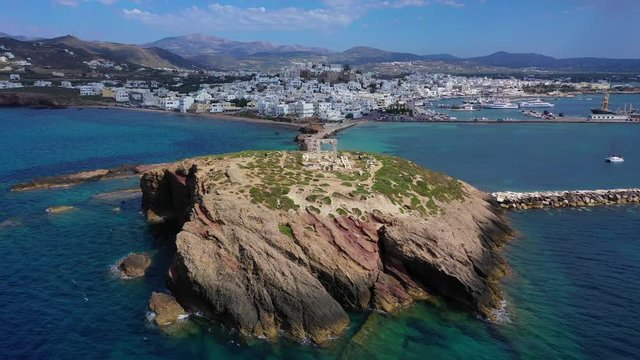 Aerial drone panoramic view video of iconic and unique Temple of Apollon or Portara (Gate) with breathtaking views to port - town and castle of Naxos island and the Aegean blue sea, Cyclades, Greece