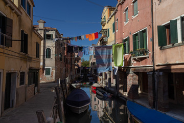 Fototapeta na wymiar Narrow Canal View with boats and clothes on the line and the typical Venetian Buildings. Venice, Italy