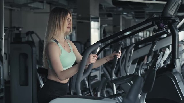 Athletic blonde woman working out on stepper machine at gym. Young slim female in fitness club. Medium shot