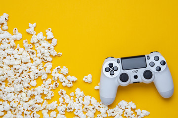 White modern gamepad on a yellow background among popcorn. © solidmaks