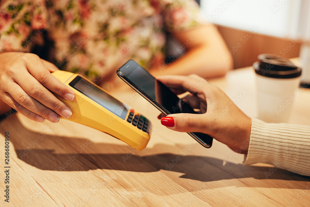 Wall mural Woman paying with NFC technology on mobile phone, restaurant, cafe, bar, clothing store