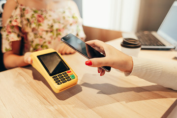 Woman paying with NFC technology on mobile phone, restaurant, cafe, bar, clothing store