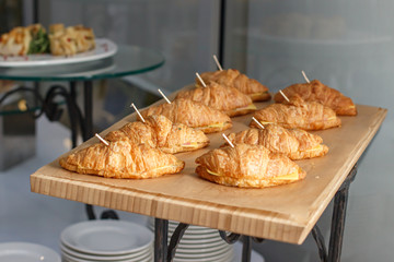 Nine croissants with cheese and ham on skewers.