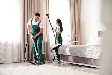 Team of janitors cleaning bedroom with professional equipment