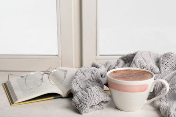 Composition with cup of hot chocolate and book on windowsill, space for text. Winter drink