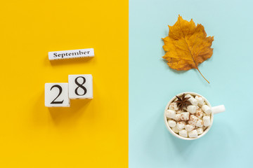 Autumn composition. Wooden calendar September 28, cup of cocoa with marshmallows and yellow autumn leaves on yellow blue background. Top view Flat lay Mockup Concept Hello September.