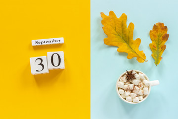 Autumn composition. Wooden calendar September 30, cup of cocoa with marshmallows and yellow autumn leaves on yellow blue background. Top view Flat lay Mockup Concept Hello September.