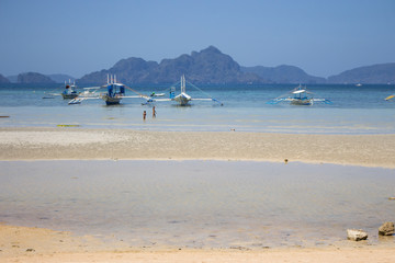 El Nido, Palawan, Philippines - 03/02/2019: two unknown children playing on the beach with boats. Scenic tropical landscape with island on horizon. Traditional philippines boats on sea coast. 