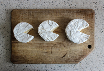 Three heads of cheese, with white mold, on a wooden surface. Delicious brie, Camembert, goat. Form round without one segment is incised.