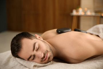 Obraz na płótnie Canvas Handsome man receiving hot stone massage in spa salon. Space for text