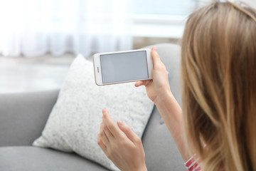 Young woman using video chat on smartphone in living room, closeup. Space for design