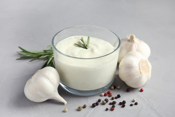 Obraz na płótnie Canvas Fresh garlic bulbs, bowl of sauce, rosemary and pepper on grey background