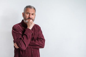 Half-length portrait of a serious gray-haired bearded man in a burgundy shirt on a white background