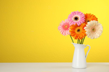 Bouquet of beautiful bright gerbera flowers in vase on table against color background. Space for text