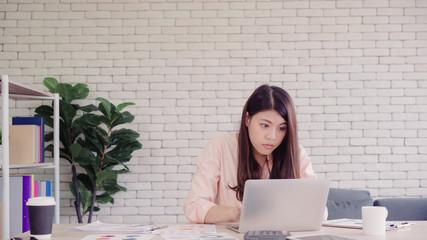 Beautiful young smiling asian woman working laptop on desk in living room at home. Asia business woman writing notebook document finance and calculator in home office. Enjoying time at home concept.