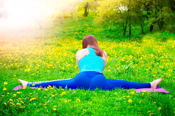 Girl practicing stretching exercises. Beautiful young women doing stretching exercise on green grass at park.Back view.