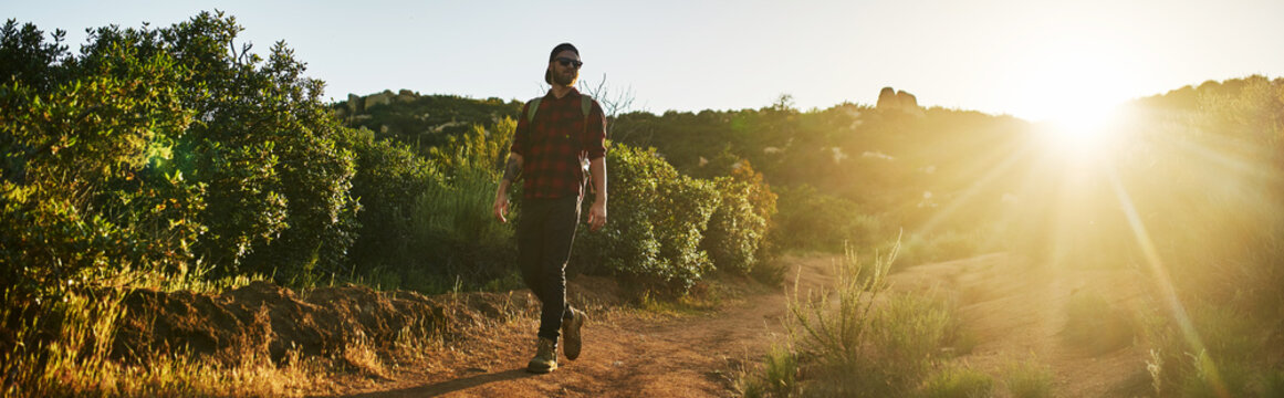 bearded millennial hiker walking trail with backpack during sunset