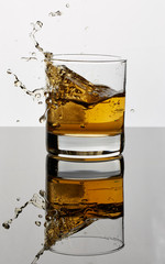 Golden brown liquor splashing with ice in a glass and reflecting on the table’s surface